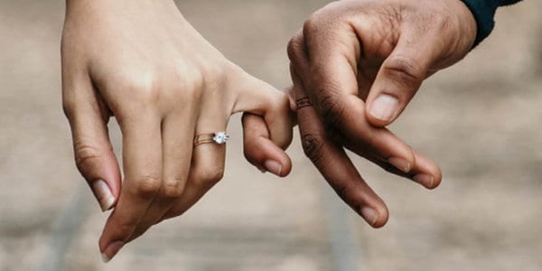 Two hands with pinkies locked, woman with wedding ring, man with ring tattoo with maple leafs.