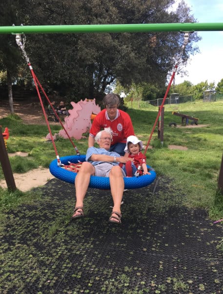 Grandfather and grandchild on swing being pushed by her dad.