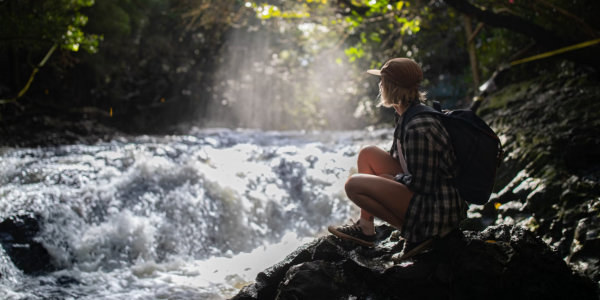 Woman with backpack sitting beside river