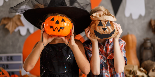 Two people with Halloween-themed candy collection containers in front of their faces